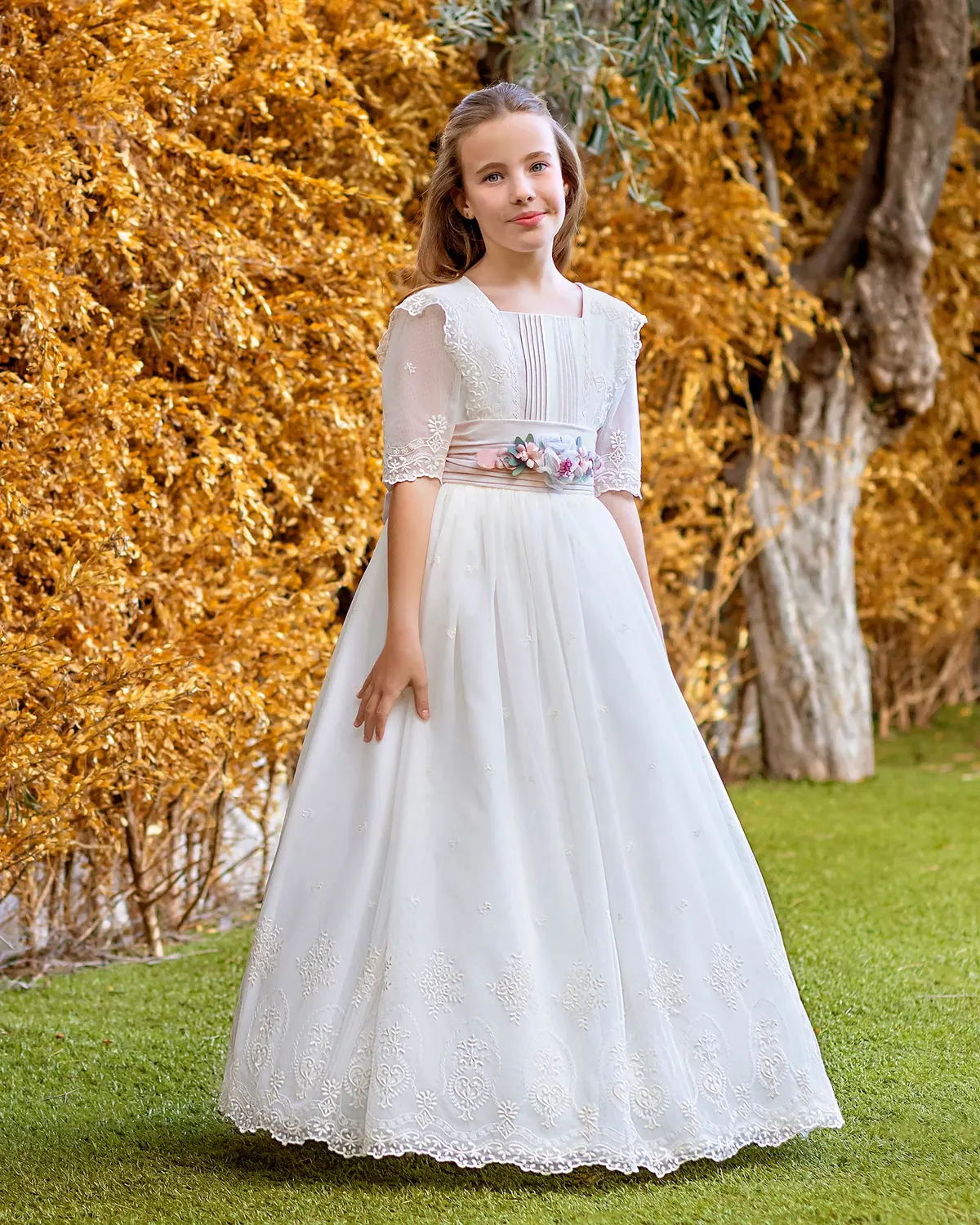 Vestido de comunión Aire Barcelona A757 de frente: pechera de alforzas, fajín rosa con flores y falda bordada