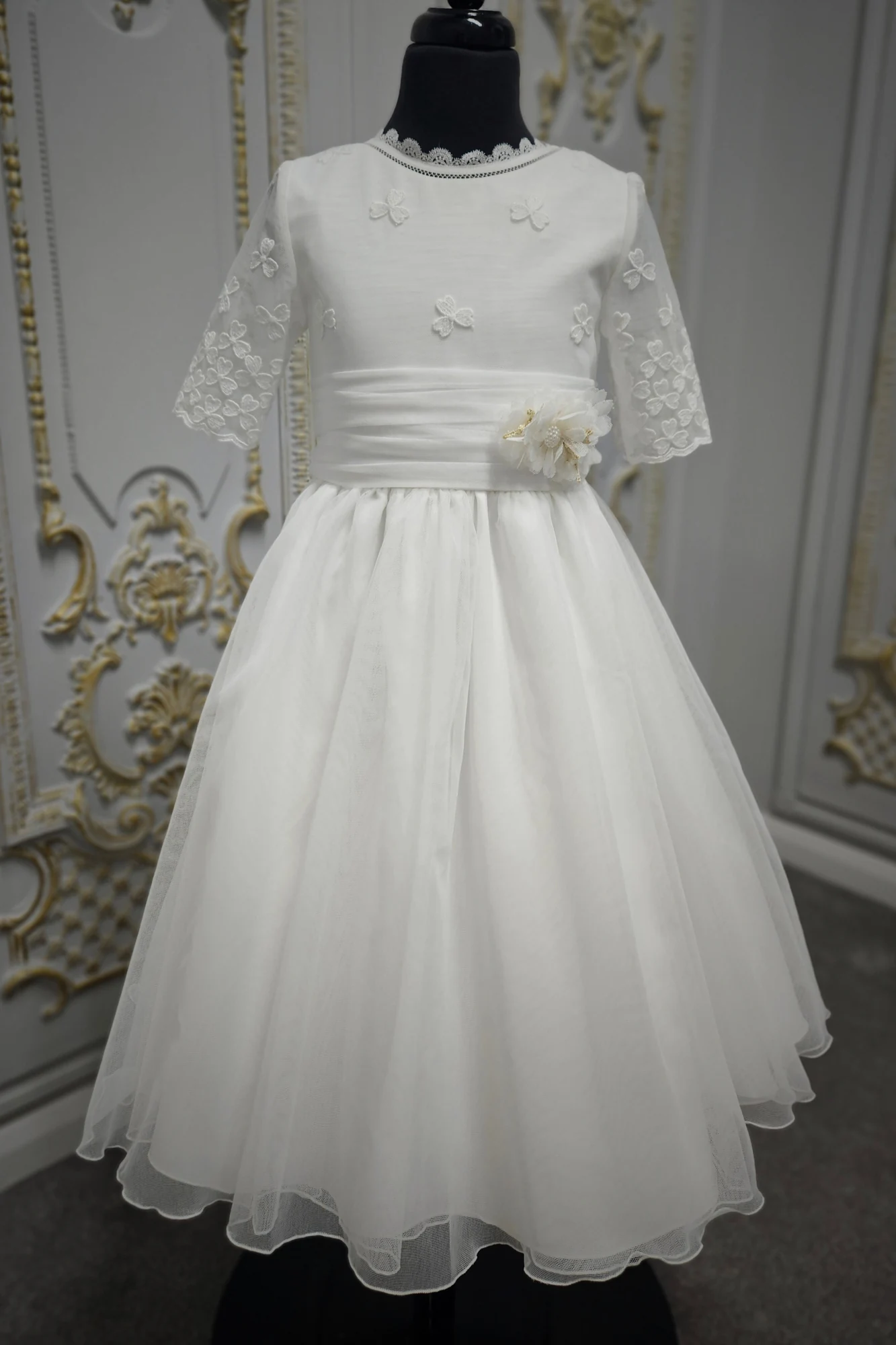 Vestido de comunión Carmy 5203 en maniquí, de frente: apliques de tréboles, fajín con flor y falda de tul