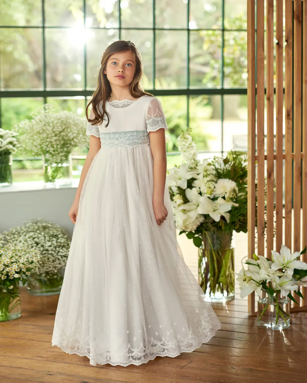 Vestido de comunión Rosa Clará First R606 de frente: talle imperio, fajín de encaje azul empolvado y falda bordada