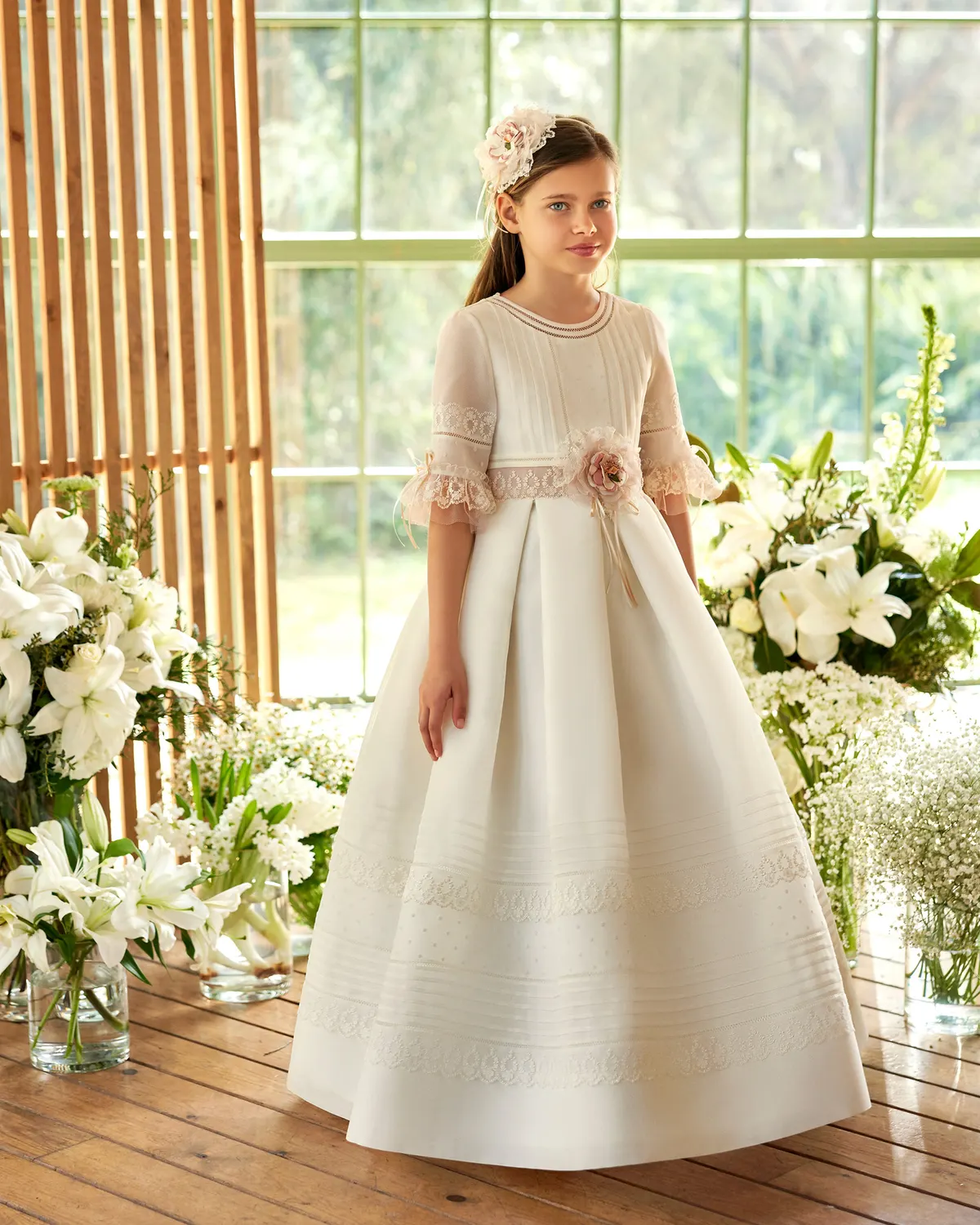 Vestido de comunión Rosa Clará First R612 de frente: manga con volante rosa, cinturilla con flor y falda de tablas