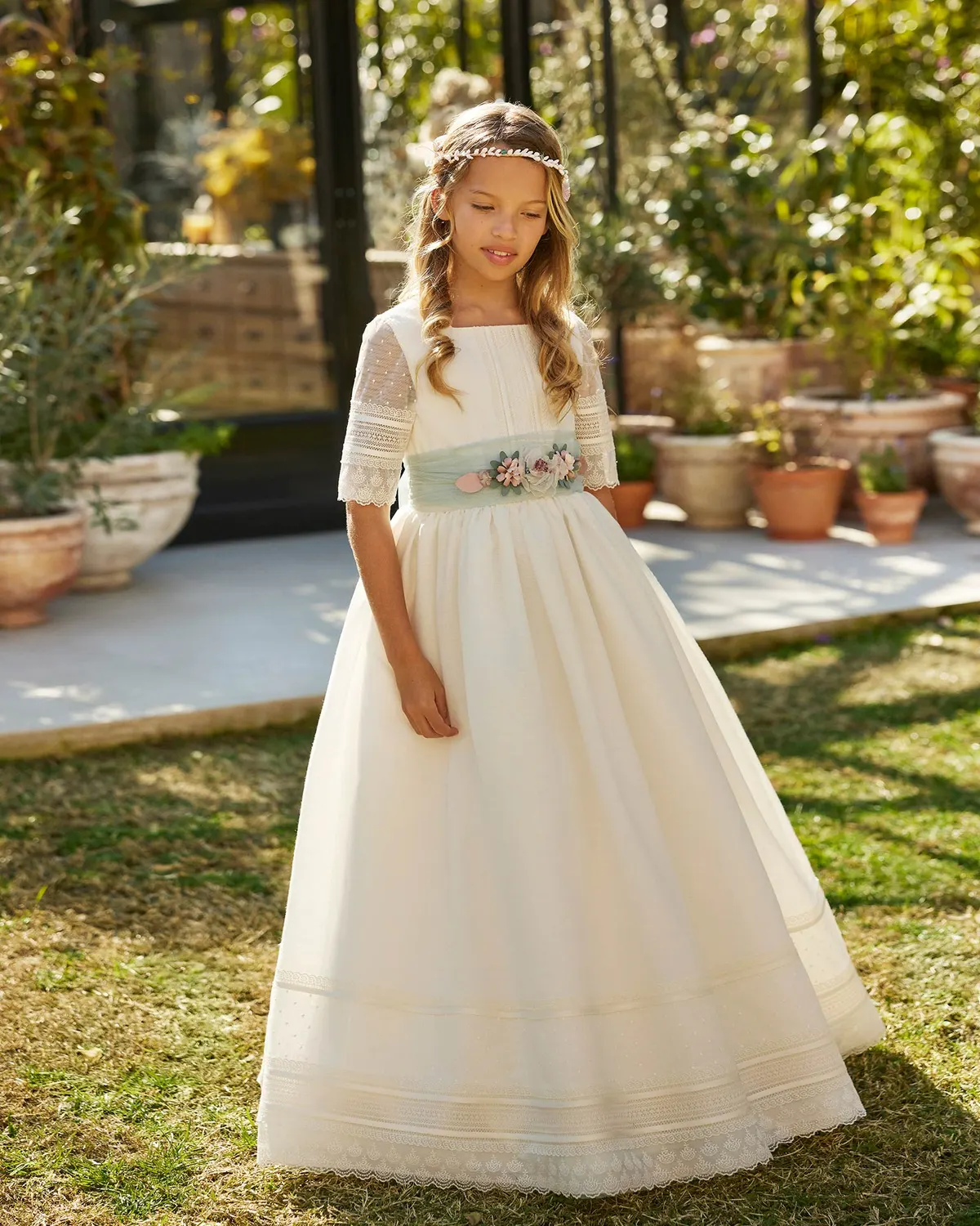 Vestido de comunión Rosa Clará First R716 de frente: escote cuadrado, fajín verde agua con flores y falda con cenefas